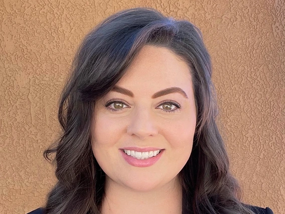 erica travassos, medium length brown hair, smiling, wearing a black blazer and colorful red blouse