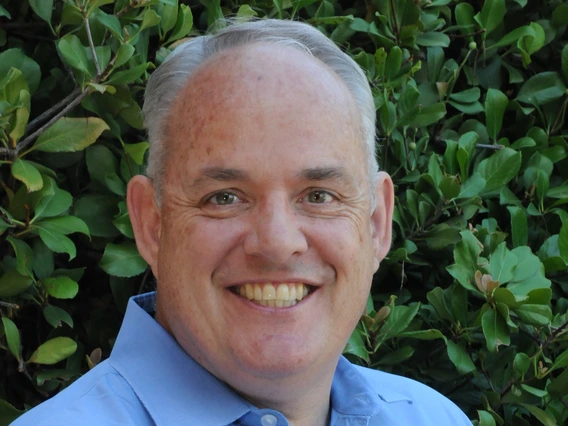 michael griffith wearing a blue button up shirt standing in front of green foliage