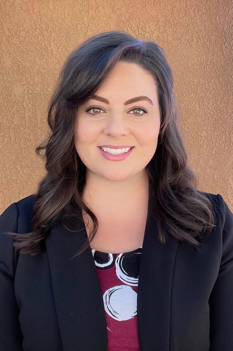 erica travassos, medium length brown hair, smiling, wearing a black blazer and colorful red blouse