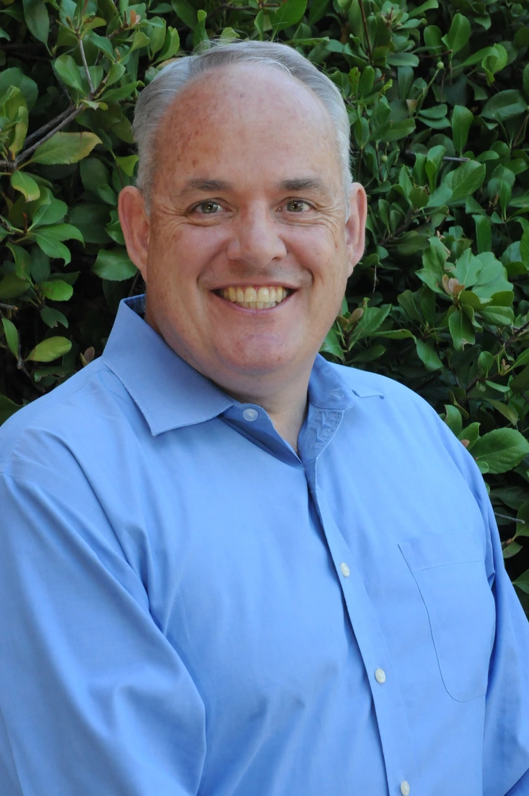 michael griffith wearing a blue button up shirt standing in front of green foliage
